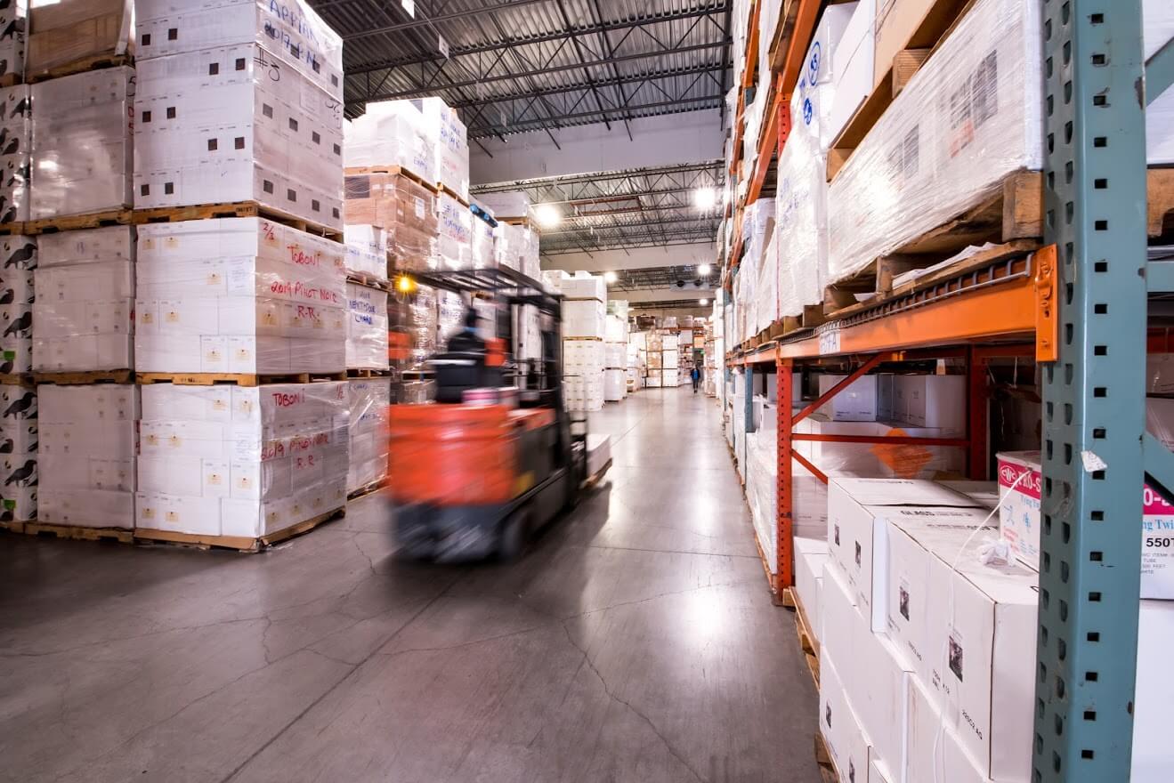 Blurred image of a forklift passing through racks in a wine warehouse.